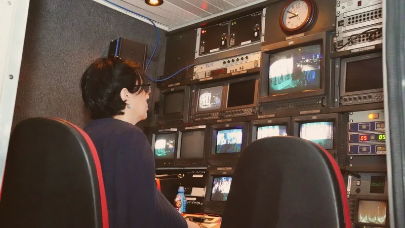 Photograph of a television production gallery — a wall of monitors and a vision-mixing desk, with no people in frame.