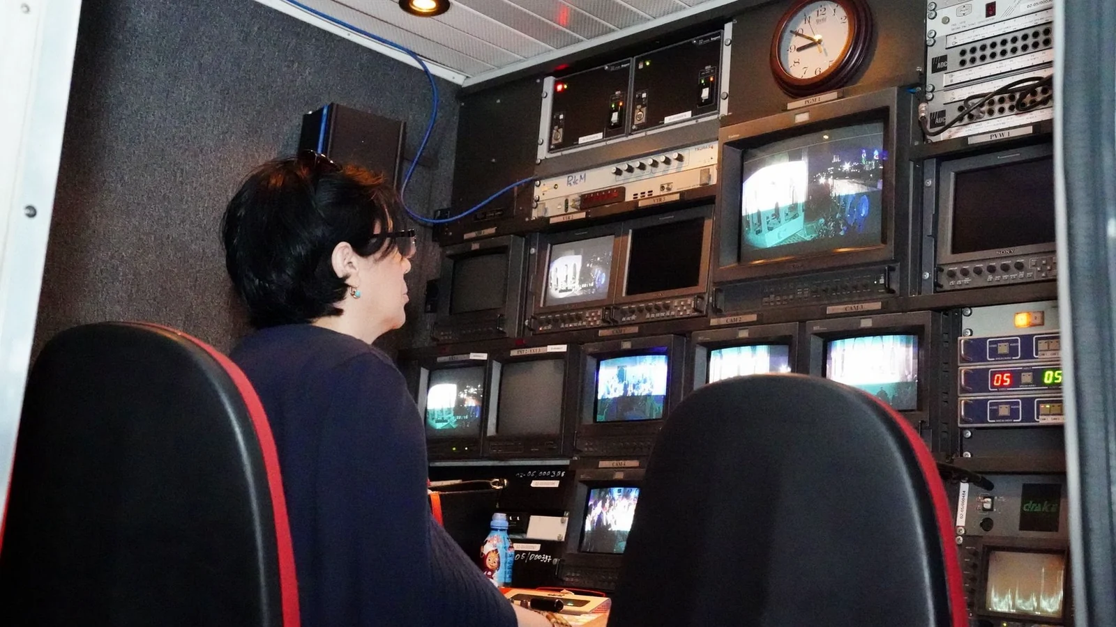A television gallery with a wall of monitors and a vision mixing desk, racing graphics on the preview row.